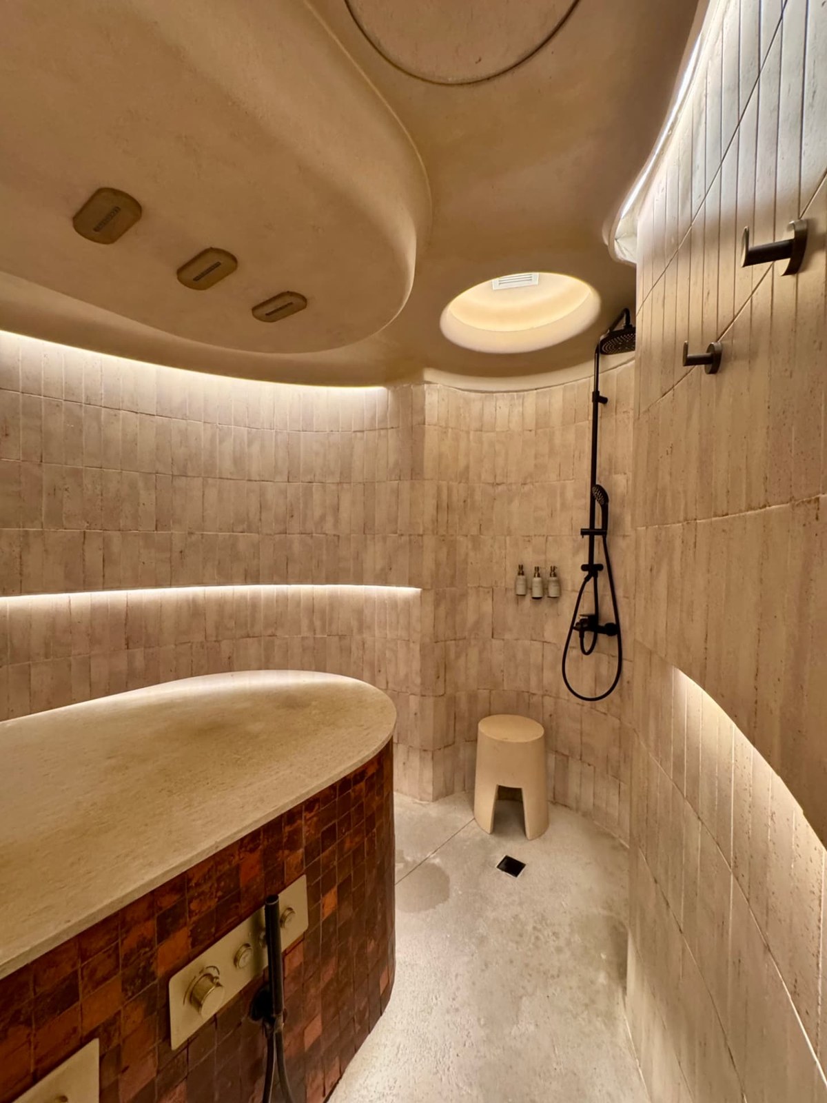 A curved spa bathing room with warm plaster walls, a mosaic-sided tub and an overhead skylight