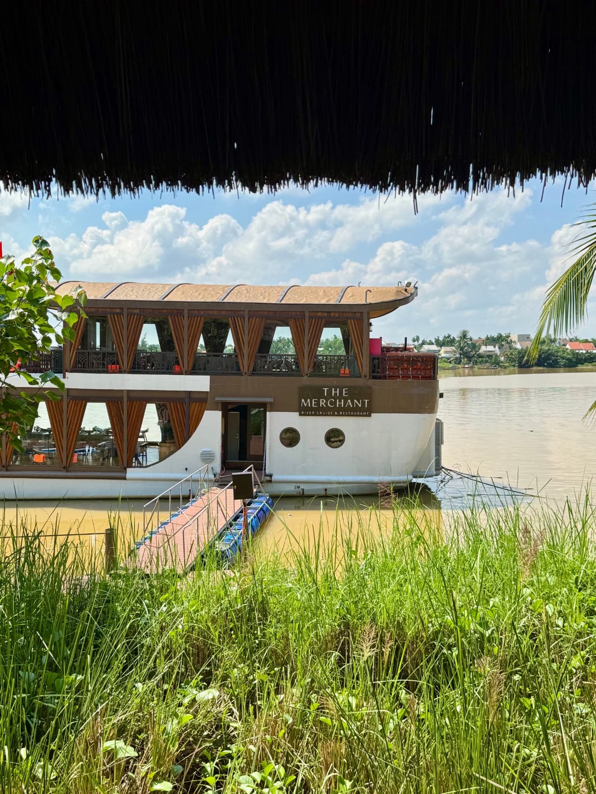 The Merchant river cruise and restaurant moored beside the resort, seen beneath a thatched roof