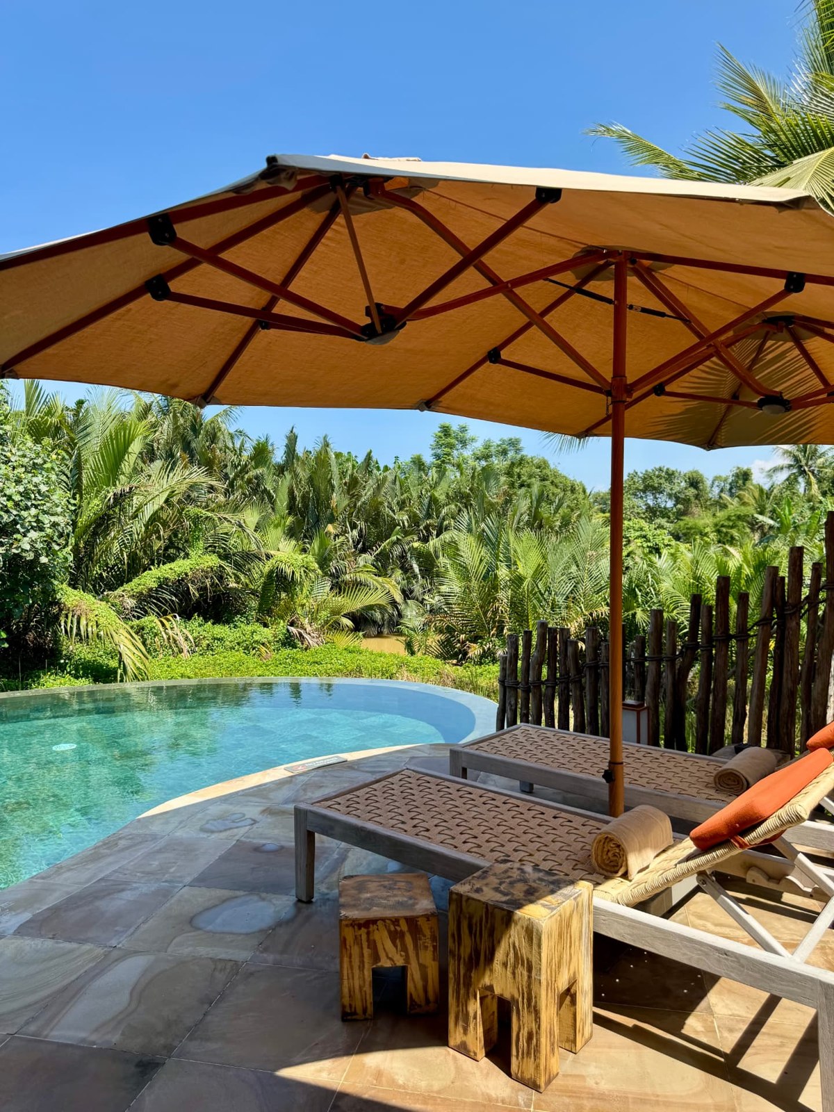 A private pool and timber loungers beneath a parasol, surrounded by lush palms at the retreat resort